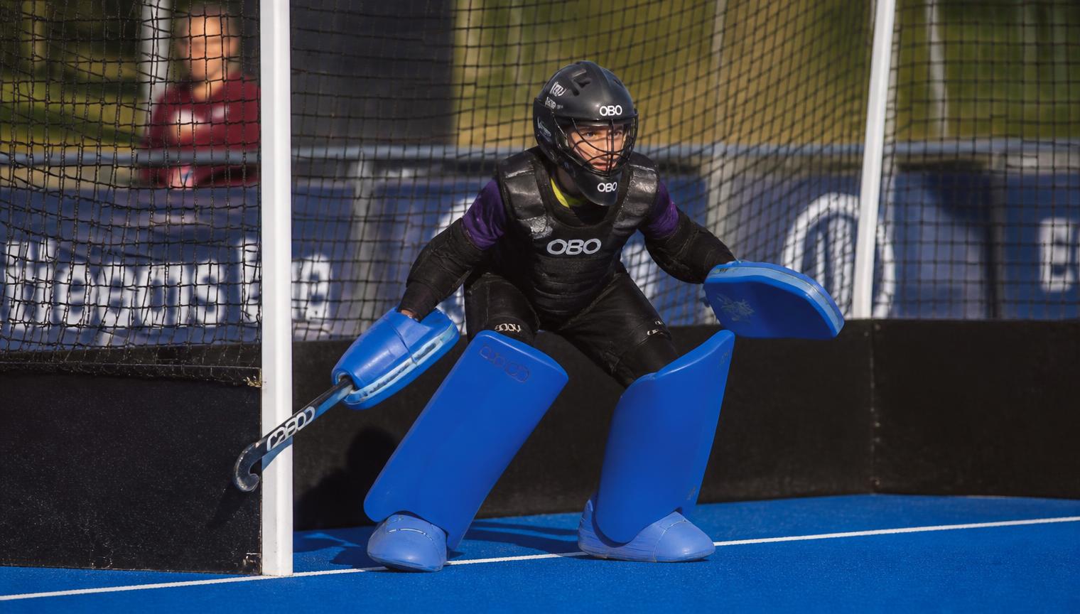 Jeugdkeeper in vol tenue klaar in het doel op een blauw kunstgrasveld