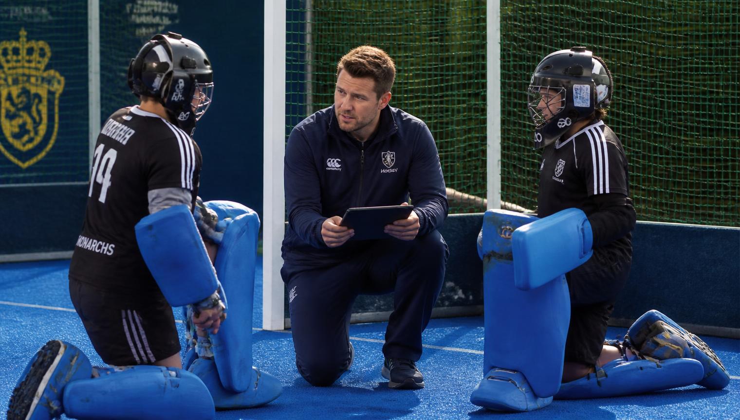 Keepertrainer met tablet in gesprek met twee jeugdkeepers naast het doel